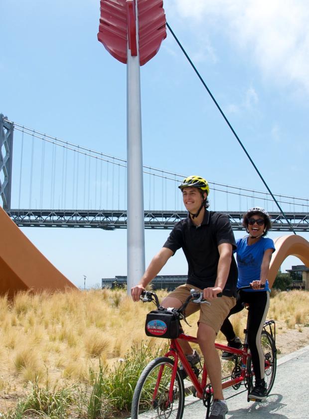 Tandem team riding in front of Cupid's Span and the Bay Bridge on a beautiful clear day!