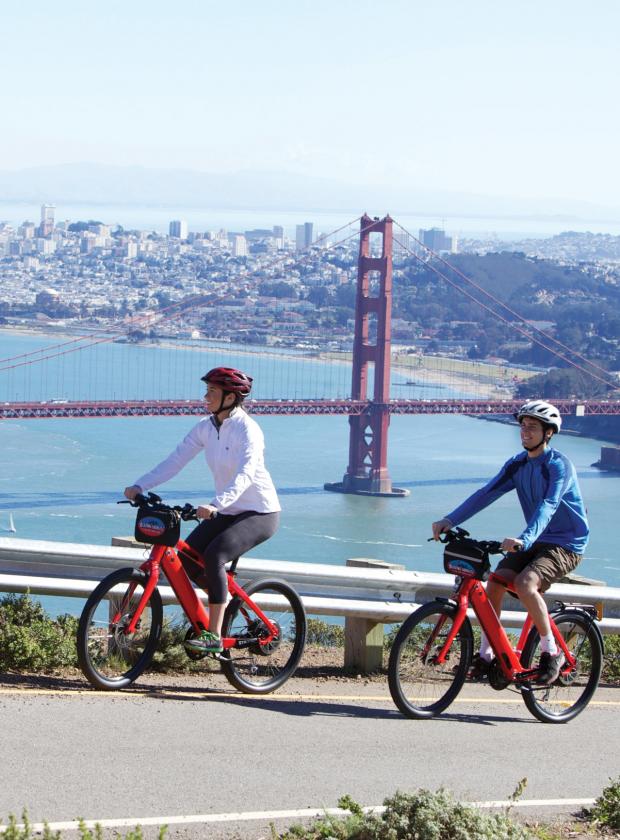 Couple riding electric bikes up Hawk Hill with stunning views of Golden Gate Bridge and San Francisco
