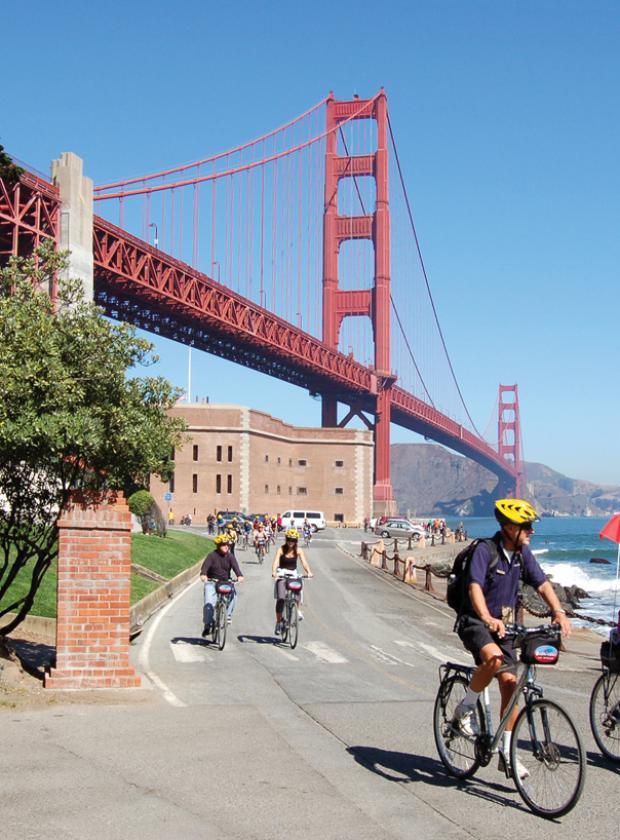Guided bike tour riding under the Golden Gate Bridge near historic Fort Point