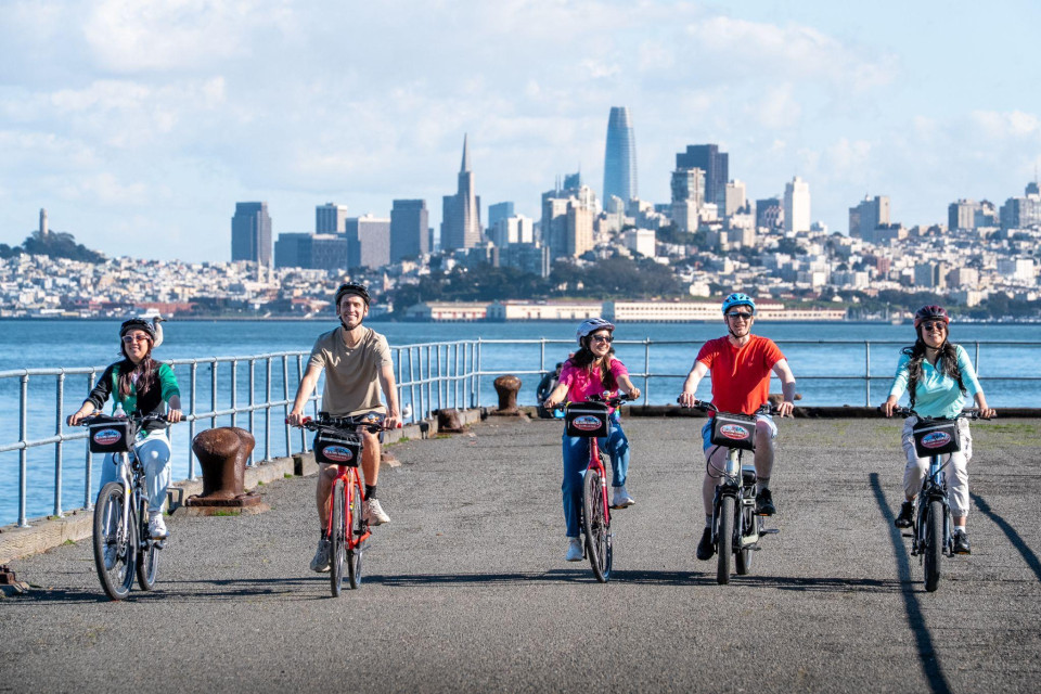 Family riders on a waterfront path with the city skyline behind them