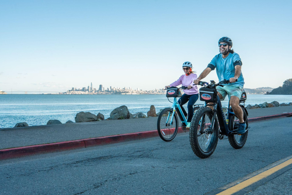 Two riders getting comfortable on electric bikes along the bay