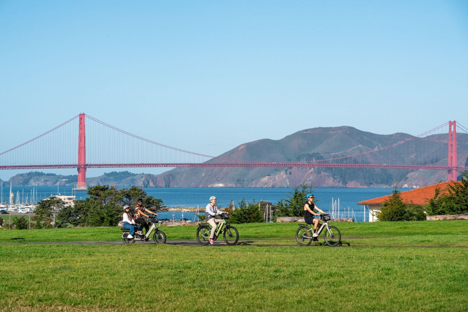 Family riders on a park path with the Golden Gate Bridge in the background