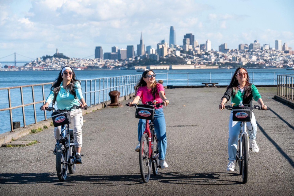 Small riding group on a flat waterfront segment before heading toward the bridge