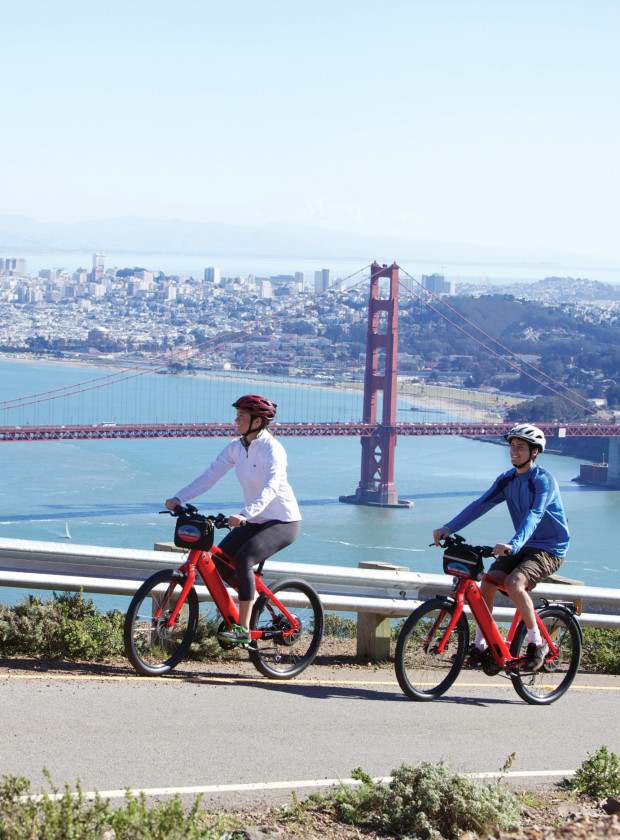 Couple riding electric bikes up Hawk Hill with stunning views of Golden Gate Bridge and San Francisco